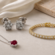 Jewelry set featuring a silver necklace with a red gemstone pendant, diamond cluster stud earrings, and a gold tennis bracelet
